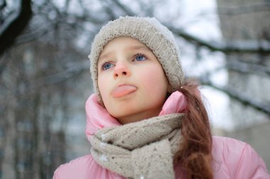 Kışın karla oynayan, dille kar yiyen ve kış kıyafetleriyle açık havada gözlerini kapatan bir kız. Mutlu çocukluklar ve aktif tatiller.
