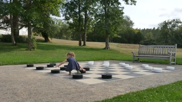 Little girl is playing large outside checkers in the park. Active child, happy childhood concepts — Stock Video