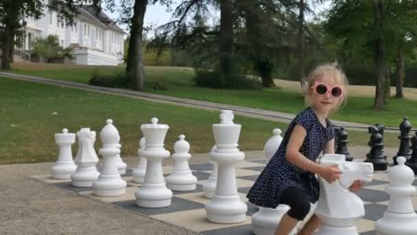 Klein meisje speelt groot schaak buiten in het park. Actief kind, gelukkige jeugdconcepten — Stockvideo