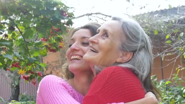 Madre anziana con i capelli grigi con la figlia adulta che guarda la telecamera in giardino e si abbraccia durante la giornata di sole all'aperto — Video Stock