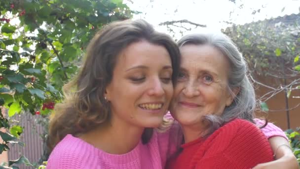 Madre mayor con el pelo gris con su hija adulta se están abrazando durante el día soleado al aire libre en el jardín — Vídeo de stock