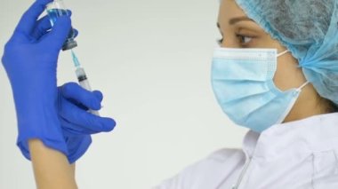 Mavi koruyucu eldivenli kadın doktorların elleri kliniğin beyaz arka planında aşıya hazırlanıyor..