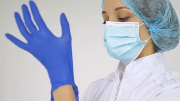 Vrouwelijke arts trekt beschermende blauwe handschoenen aan en begint te bidden geïsoleerd op witte achtergrond voor sommige medische manipulaties, vaccinatie. — Stockvideo