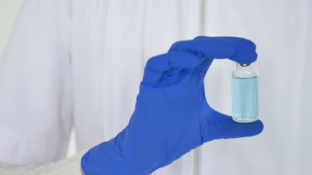 Un lucrător medical arată că vaccinul coronavirus poartă mănuși de protecție albastre pe fundalul alb al clinicii . — Videoclip de stoc