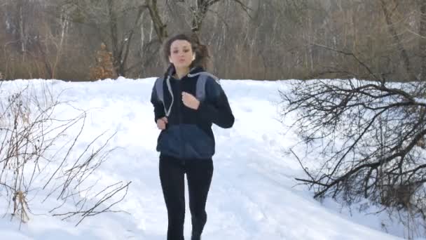 Wiosenny lub zimowy portret młodej atletycznej dziewczyny biegającej po parku w ciemnych strojach sportowych na drzewach ze śnieżnym tłem. Koncepcja zdrowego stylu życia. — Wideo stockowe