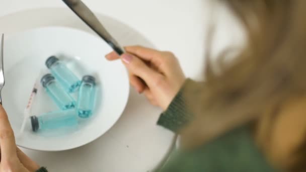 Kvinna kommer att äta från vit platta med glasampuller med blå vätska inuti, vaccinationskoncept, ovanifrån — Stockvideo