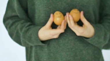Yeşil kazaklı genç bir kadın antropomorfik gülen yüzlü iki el çizimi yumurta, Paskalya hazırlığı, tatil ruh hali konseptleri gösteriyor.