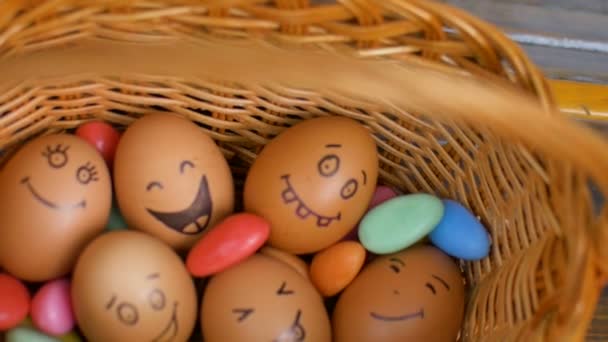Stos ręcznie rysowane jajka smiley na słomkowym koszu z kolorowymi cukierkami, przygotowanie wielkanocne, świąteczne koncepcje nastroju — Wideo stockowe