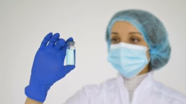 Bir sağlık görevlisi, kliniğin beyaz arka planında mavi koruyucu eldiven takan koronavirüs aşısını gösteriyor..