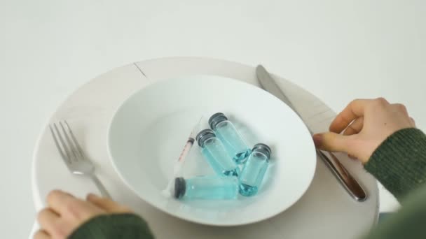 Frau isst von weißem Teller mit Glasampullen mit blauer Flüssigkeit im Inneren, Impfkonzept, Draufsicht — Stockvideo