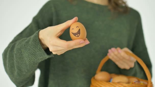 Jovem fêmea em camisola verde está mostrando ovos desenhados à mão com rosto sorridente antropomórfico da cesta de palha, preparação de Páscoa, conceitos de humor de férias — Vídeo de Stock