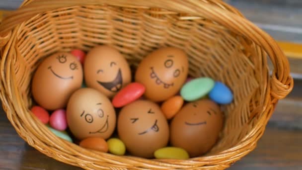 Пачка яиц с нарисованными от руки лицами на соломенной корзине с красочными конфетами, подготовка к Пасхе, праздничное настроение — стоковое видео
