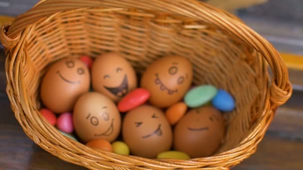 Пачка яиц с нарисованными от руки лицами на соломенной корзине с красочными конфетами, подготовка к Пасхе, праздничное настроение — стоковое видео