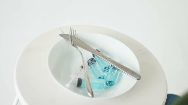 Frau isst von weißem Teller mit Glasampullen mit blauer Flüssigkeit im Inneren, Impfkonzept, Draufsicht — Stockvideo