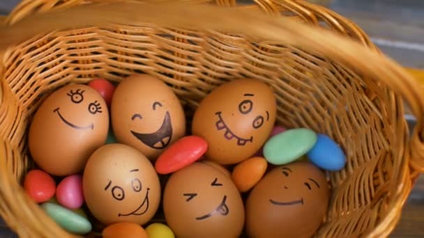 Pila de huevos con caras dibujadas a mano en canasta de paja con dulces de colores, preparación de Pascua, conceptos de humor de vacaciones — Vídeo de stock