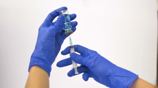 Hälso- och sjukvårdspersonal slår in vaccinet från ampullen i en spruta med blå skyddshandskar — Stockvideo