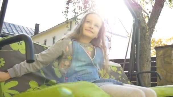Bambina bionda che si diverte su un'altalena all'aperto durante la giornata di sole estiva nel parco giochi in giardino, concetto di infanzia felice — Video Stock
