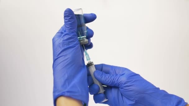 Hälso- och sjukvårdspersonal slår in vaccinet från ampullen i en spruta med blå skyddshandskar — Stockvideo