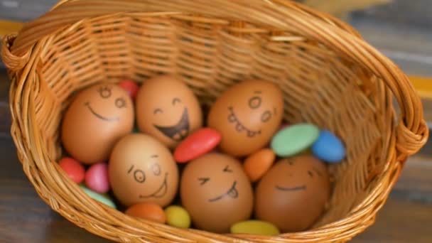 カラフルなキャンディー、イースターの準備、休日の気分の概念を持つわらバスケットに手描きの顔を持つ卵のスタック — ストック動画