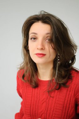 Kırmızı örgü süveter ve beyaz arka planda küpe giyen genç bir kadının stüdyo portresi.