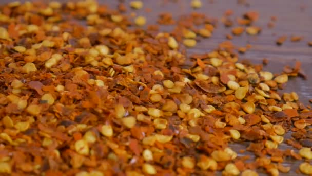 Czerwony gorący płatek papryki chili spada na drewniany stół. Koncepcja gotowania, przyprawy do jedzenia, zbliżenie — Wideo stockowe