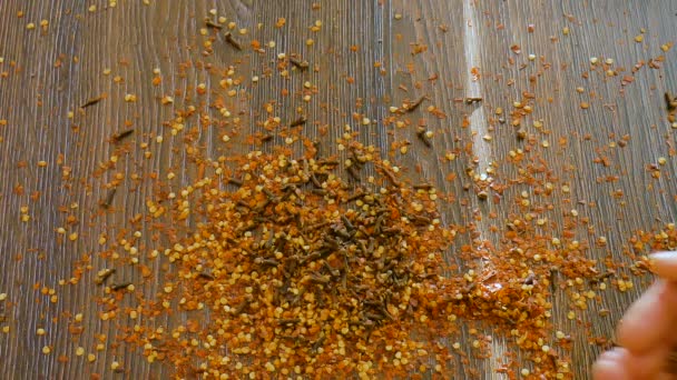 Especias sin clasificar en la mesa de madera, semillas de lino están cayendo de las manos femeninas, condimentos para la comida. Vista superior de la hojuela de chile rojo picante, pimentón, clavo de olor, semillas. — Vídeo de stock