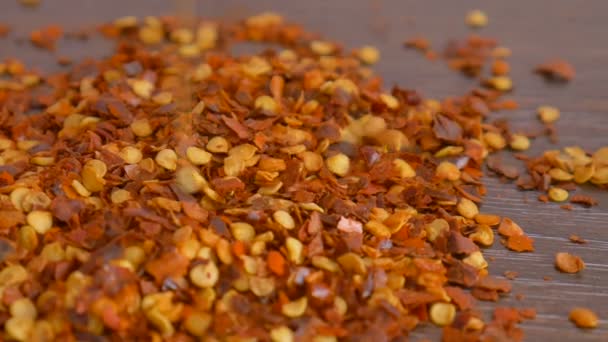 Vörös csípős chilis paprikapehely esik le a fa asztalra. Főzési koncepció, ételízesítők, közelkép — Stock videók