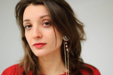 Kırmızı örgü süveter ve beyaz arka planda küpe giyen genç bir kadının stüdyo portresi.