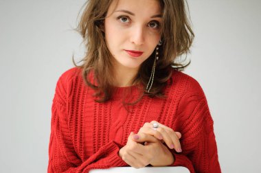 Kırmızı örgü süveter ve beyaz arka planda küpe giyen genç bir kadının stüdyo portresi.