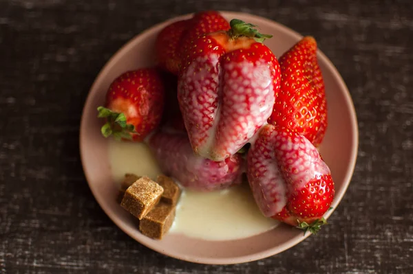 Morangos vermelhos maduros em placa redonda com alguns pedaços de açúcar de cana e chocolate branco derretido — Fotografia de Stock