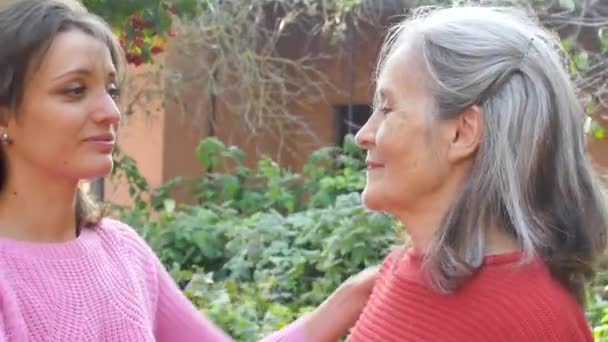 Senior moeder met grijs haar met haar volwassen dochter knuffelen elkaar tijdens zonnige dag buiten in de tuin — Stockvideo