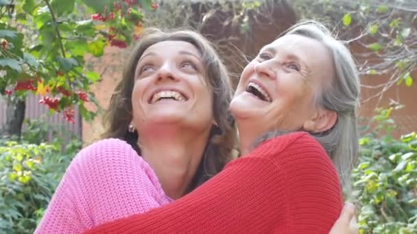 Mãe sênior com cabelos grisalhos com sua filha adulta estão abraçando uns aos outros durante o dia ensolarado ao ar livre no jardim — Vídeo de Stock