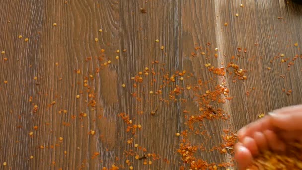 Válogatatlan fűszerek a fa asztalon, vörös csípős chili paprika pehely esik le a női kéz, fűszerek élelmiszer. — Stock videók