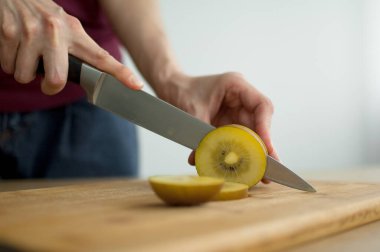 Dişi eller kesilmiş bir tahta üzerinde taze, olgun bir altın kivi meyvesini kesiyor. Egzotik meyveler, sağlıklı beslenme konsepti