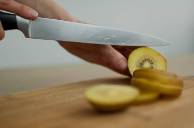 Dişi eller kesilmiş bir tahta üzerinde taze, olgun bir altın kivi meyvesini kesiyor. Egzotik meyveler, sağlıklı beslenme konsepti