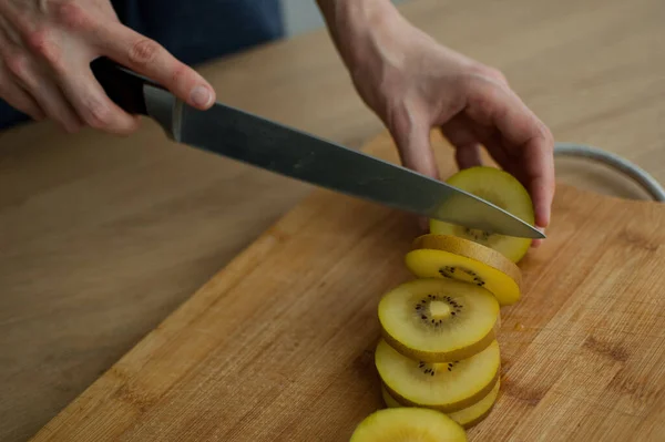 Le mani femminili stanno tagliando un kiwi dorato maturo fresco su un tagliere di legno. Frutti esotici, concetto di alimentazione sana — Foto Stock