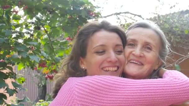 Madre mayor con el pelo gris con su hija adulta se están abrazando durante el día soleado al aire libre en el jardín — Vídeo de stock