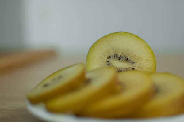 Fatias de kiwi dourado com polpa amarela em placa branca na cozinha. Frutas exóticas, conceito de alimentação saudável — Fotografia de Stock