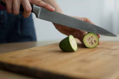 Dişi eller kesilmiş bir tahta üzerinde taze yeşil bir feijoa meyvesi kesiyor. Egzotik meyveler, sağlıklı beslenme konsepti