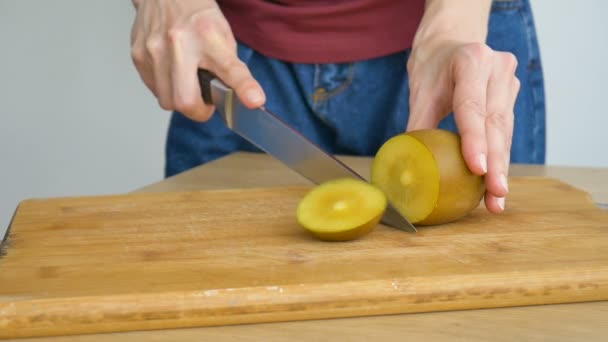 Las manos femeninas están cortando una fruta fresca madura de kiwi dorado en una tabla de madera cortada. Frutas exóticas, concepto de alimentación saludable — Vídeo de stock