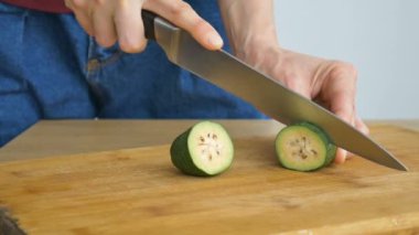 Dişi eller kesilmiş bir tahta üzerinde taze yeşil bir feijoa meyvesi kesiyor. Egzotik meyveler, sağlıklı beslenme konsepti