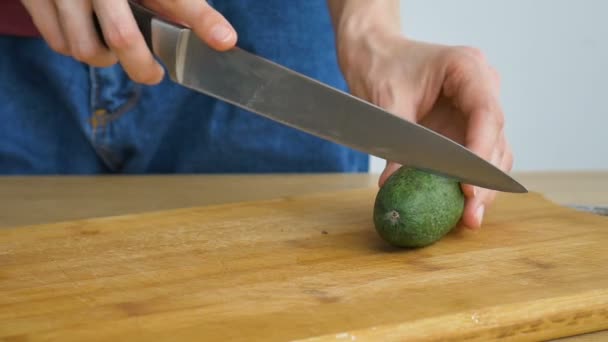 As mãos femininas estão cortando uma fruta fresca de feijoa verde em uma tábua de madeira cortada. Frutas exóticas, conceito de alimentação saudável — Vídeo de Stock