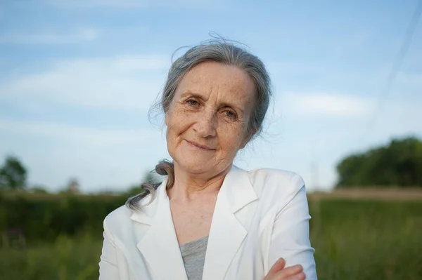 Портрет пожилой женщины с седыми волосами и лицом с морщинами в белой куртке и отдыхом в парке в солнечный день — стоковое фото