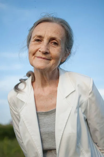 Retrato de mujer mayor con el pelo gris y la cara con arrugas con chaqueta blanca y relajarse en el parque durante el día soleado —  Fotos de Stock