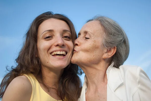 Senior mother with gray hair with her adult daughter looking at the camera in the garden and hugging each other during sunny day outdoors — Stock Photo, Image