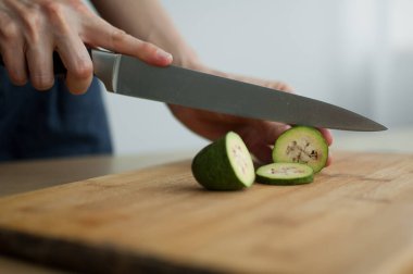 Dişi eller kesilmiş bir tahta üzerinde taze yeşil bir feijoa meyvesi kesiyor. Egzotik meyveler, sağlıklı beslenme konsepti