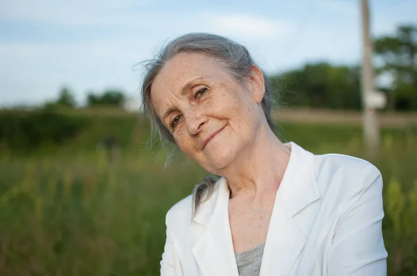 Retrato de mujer mayor con el pelo gris y la cara con arrugas con chaqueta blanca y relajarse en el parque durante el día soleado — Foto de Stock