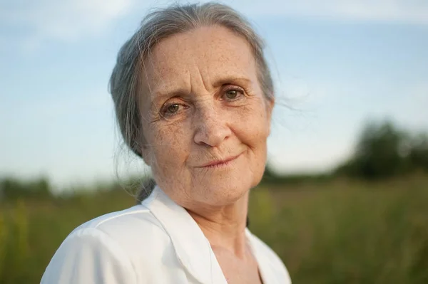 Portret van oudere vrouw met grijs haar en gezicht met rimpels in witte jas en ontspannen in het park tijdens de zonnige dag — Stockfoto