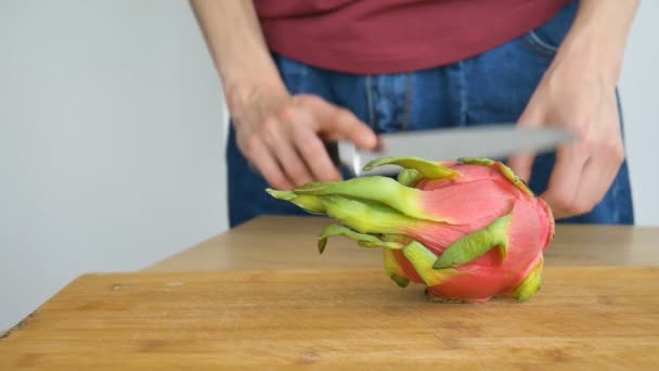Vrouwelijke handen is het snijden van een draak fruit of pitaya met roze huid en witte pulp met zwarte zaden op houten snijplank op de tafel. Exotische vruchten, gezond eten concept — Stockvideo