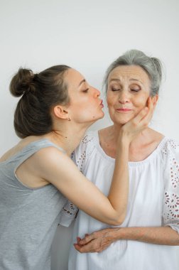 Mutlu kıdemli anne yetişkin kızına sarılıyor, kadınlar birlikte gülüyor, farklı nesillerden gelen samimi aile beyaz arka planda eğleniyor.